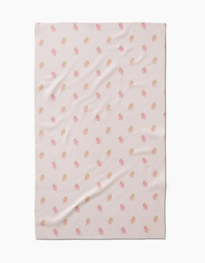 The Cindy blanket by Kelsi Fullmer features a light pink hue, subtle textured pattern, and small pink and green floral motifs. Made from recycled materials, it’s shown laid flat with slight creases.