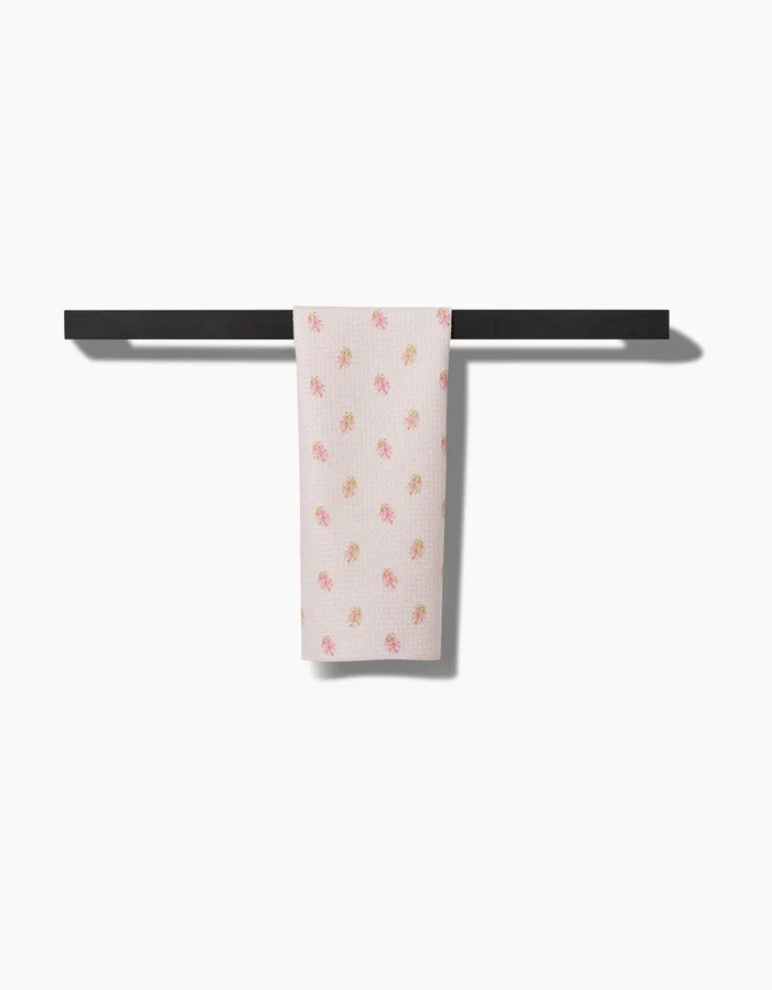 The Cindy bar towel by Kelsi Fullmer, made from recycled materials and decorated with small pink and yellow flowers, hangs neatly on a simple black towel bar against a plain white background.