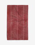 The Becki Owens Cinnamon tea towel is a red, rectangular, ultra-absorbent kitchen towel made from recycled materials. It features four thin white vertical stripes, visible creases, and a subtle mottled texture.