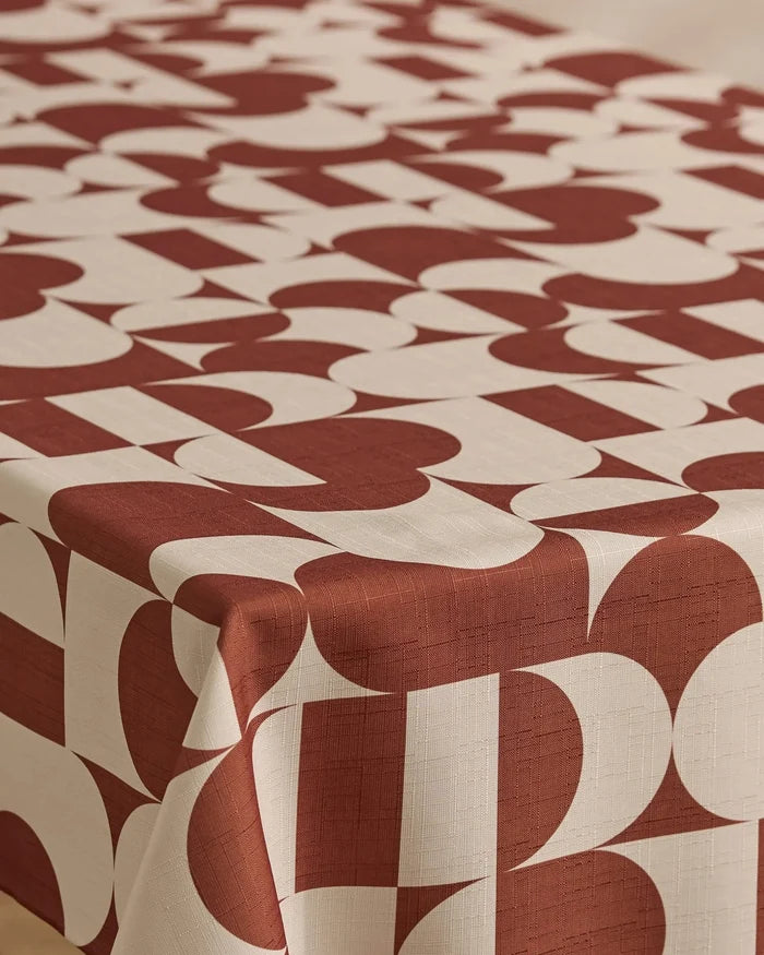 A table covered with Geometry’s Circle Playground cream-colored, stain-resistant tablecloth, featuring a bold geometric pattern of large, overlapping red shapes and arches.