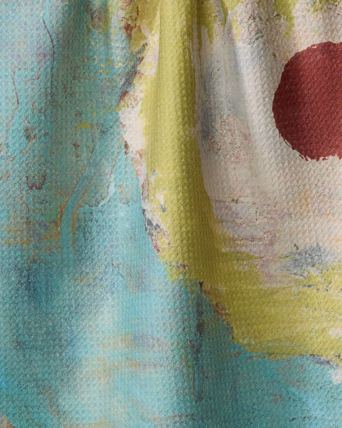 A close-up of the "Circle Squared" tea towel by Katherine Berkeley, showcasing its soft, slightly wrinkled texture and vibrant abstract pattern with blue, yellow, green, and a bold red oval on the right.
