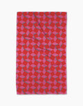 The Geometry Circus Stand Tea Towel features a red rectangular design with pink and blue interlocking cubes for a 3D optical illusion, crafted to eco-friendly standards for both style and sustainability.