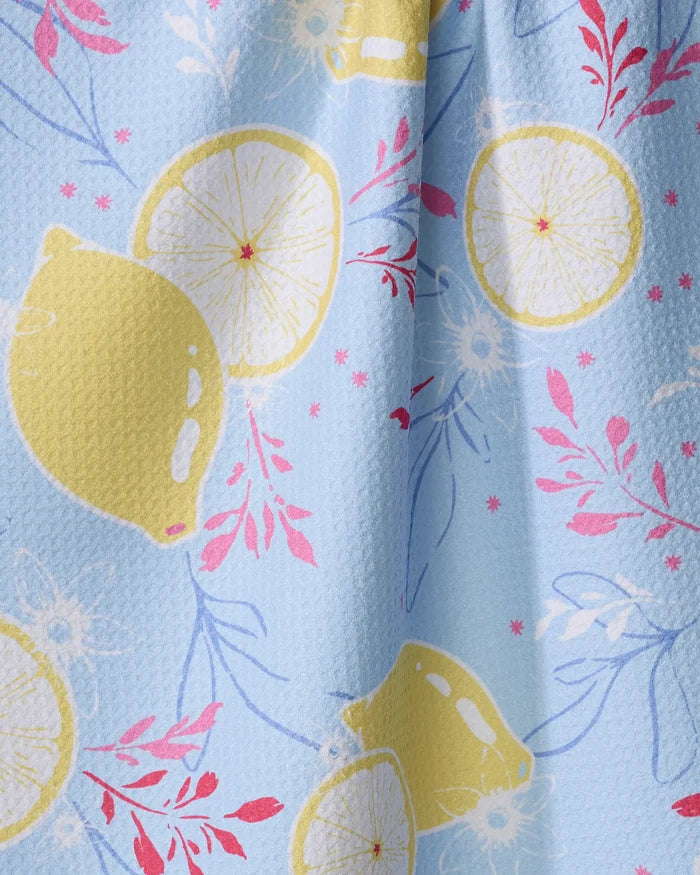 The Citrus Bloom towel by Ashley Celena is a light blue, ultra-absorbent textured towel featuring whole yellow lemons, lemon slices, and pink and blue floral designs.