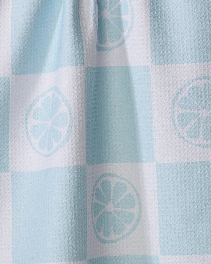 A close-up of the Citrus Blue tea towel by Janna Sue Design, featuring a light blue and white checkered pattern with repeating lemon slices. This recycled kitchen towel shows a textured surface and gentle vertical folds.