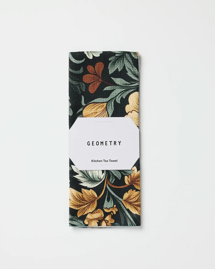 A folded eco-friendly Geometry Kitchen Tea Towel in the Classic Floral dark print with yellow, green, and rust accents, wrapped in a white label displaying the brand name. Set against a white background.
