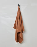 A GEOMETRY Clay waffle bath towel hangs on a black hook against a plain, light gray wall.