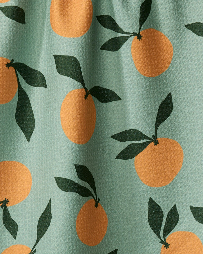 The Clementine Sky kitchen towel by Purely Kaylie features stylized oranges and dark green leaves on a light green background, crafted from recycled materials for eco-friendly appeal.
