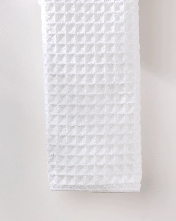 The GEOMETRY Cloud waffle hand towel, made from recycled materials, hangs vertically against a plain, light-colored wall.