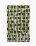 The GEOMETRY Clover Stripe tea towel features vertical olive green and white stripes with intersecting olive green blocks, shown laid flat on a white background with a slightly wrinkled fabric texture.