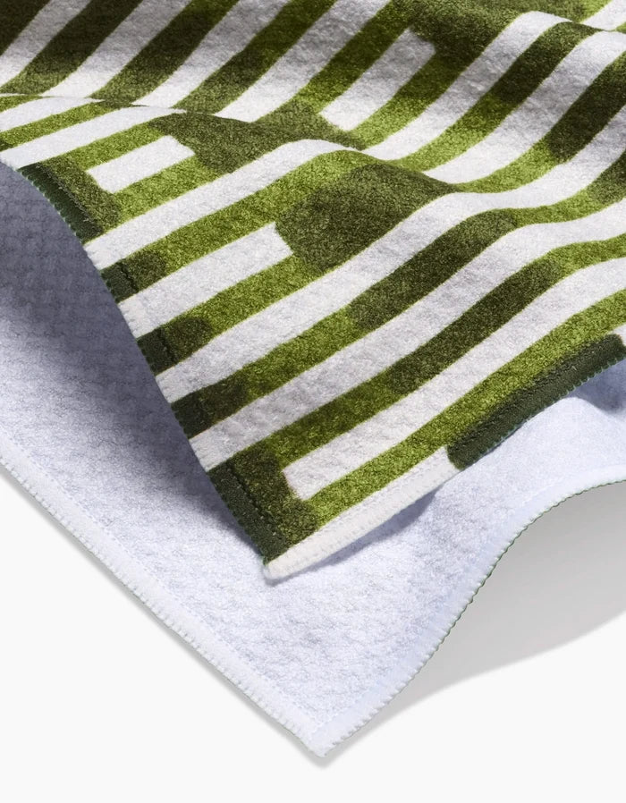 A close-up of the GEOMETRY Clover Stripe dish towel, featuring a green and white geometric stripe design on the soft front and a plain white textured back.