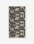 The GEOMETRY Coded bath towel is rectangular and beige, showcasing black geometric shapes—circles, squares, rectangles, and diamonds—in a repeating pattern on a white background. Made with ultra-absorbent Geoweave™ technology.