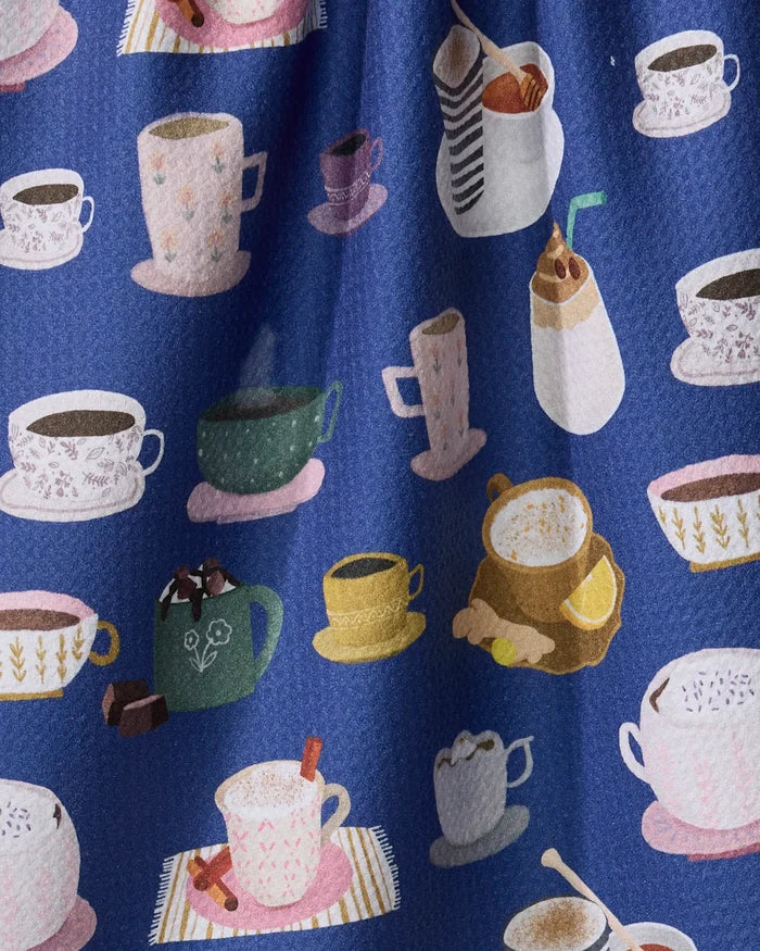 The "Coffee Drinks" kitchen towel by Cottonflower Studio features a blue design with coffee and tea cups, mugs, saucers, iced coffee, hot chocolate, and decorative accents like steam, chocolate, cinnamon sticks, and lemon slices.