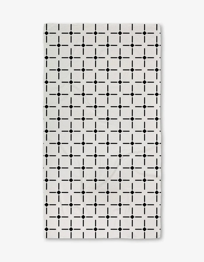 The Collins Luxe Bath Towel by Charlie Rowan Designs is a white rectangular towel featuring a repeating geometric grid of black squares and dots, crafted using innovative Geoweave technology for symmetry and style.