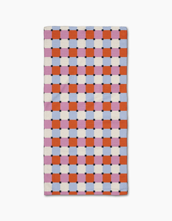 The Claire Iglesias Color Block Grid Bar Towel is crafted from Geoweave™ fabric and showcases an orange, pink, and white checkerboard pattern with blue and black accents on a crisp white background.
