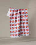 The Claire Iglesias Color Block Grid dish towel, featuring a red, orange, and blue checkered pattern, hangs neatly on a clothesline against a plain light background.