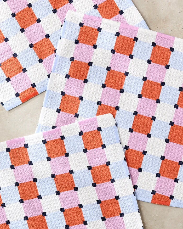 Four rectangular Claire Iglesias Color Block Grid dishcloths, featuring a colorful checkerboard pattern in red, pink, blue, white, and black squares, are arranged on a light surface. Made from recycled materials for eco-friendly use.