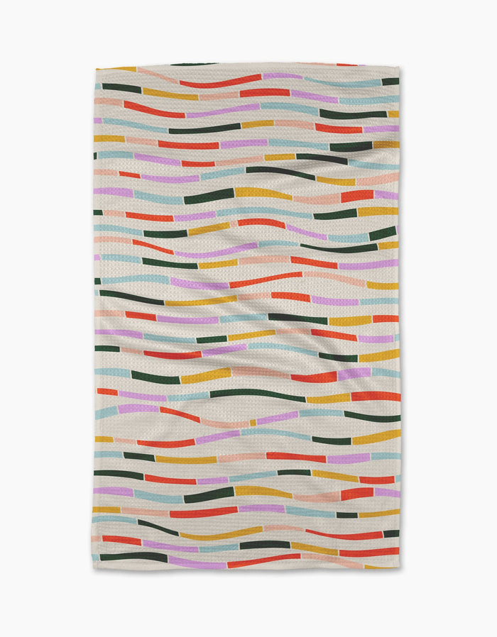 The Geometry Colorful Currents blanket features wavy, multicolored lines and rectangles in orange, pink, green, yellow, blue, and red on a light beige background. Its crafted from post-consumer recycled materials.