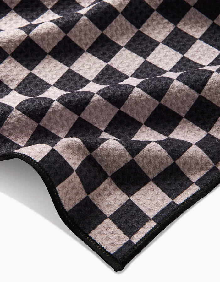 A close-up of the Geometry Cool Pup dog towel, showcasing its black and gray checkered pattern, wavy texture, stitched edge, and eco-friendly construction from recycled materials.