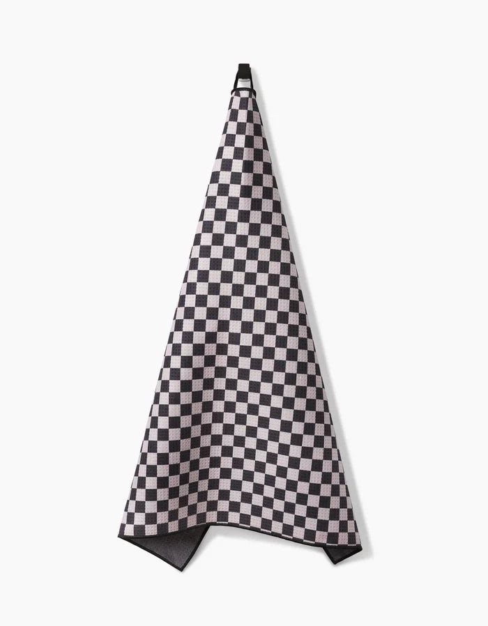 The Geometry Cool Pup towel, featuring a black and white checkered design, hangs absorbently on a hook against a plain white background.