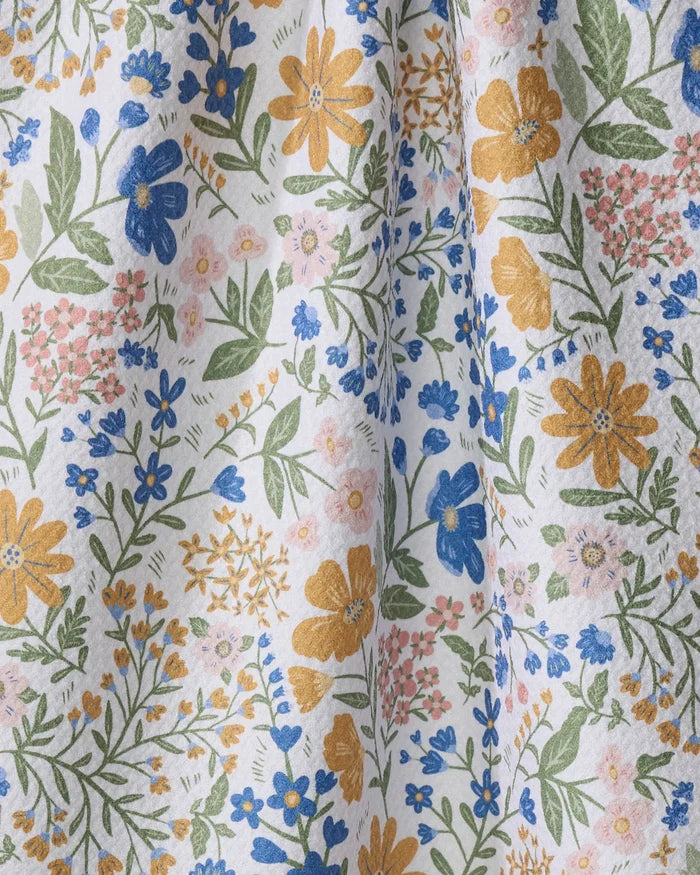 A close-up of Danelys Sidron's “Cottage Meadow Pastel” tea towel, showcasing a soft, eco-friendly fabric with yellow, blue, and pink floral patterns and green leaves on white. Gentle folds highlight its texture.