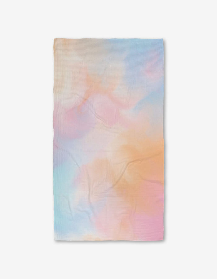 The GEOMETRY Cotton Candy Skies blanket features a soft, pastel tie-dye design in blue, pink, orange, and purple, made from post-consumer recycled materials and shown flat on a white background.
