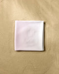 A neatly folded GEOMETRY Cotton Candy beach blanket, made from recycled materials, rests on smooth, light brown sand.