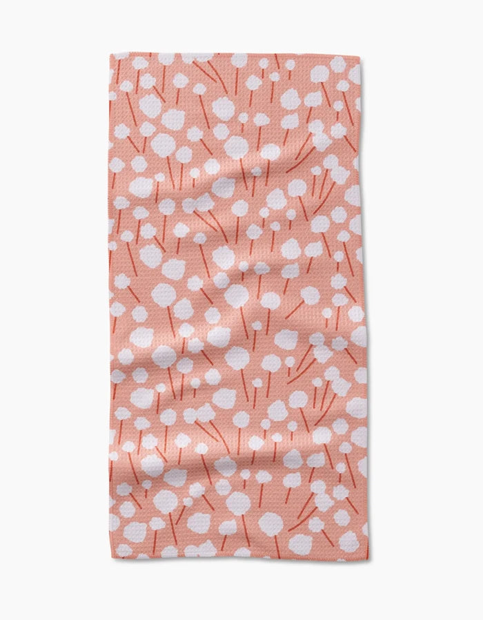 The Cotton Floral bar towel by Coit Creative features a peach hue with white dots and red lines forming abstract flowers. Made from ultra-absorbent Geoweave fabric, it’s shown laid flat with gentle wrinkles.