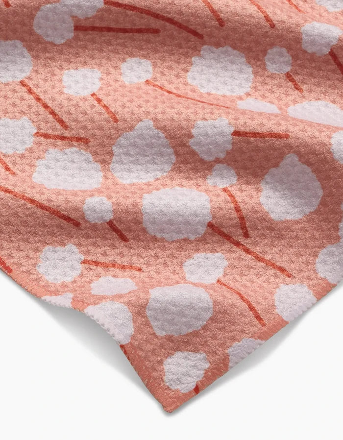A close-up of the Cotton Floral bar towel by Coit Creative, featuring ultra-absorbent Geoweave fabric with a textured pink surface, white cloud-like spots, and thin curved red lines in its floral design.
