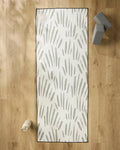 The Country Fields yoga mat by Hufton Studio, featuring gray abstract brushstrokes, rests on a light wood floor with a non-slip towel, water bottle, and two gray yoga blocks nearby for a serene workout space.