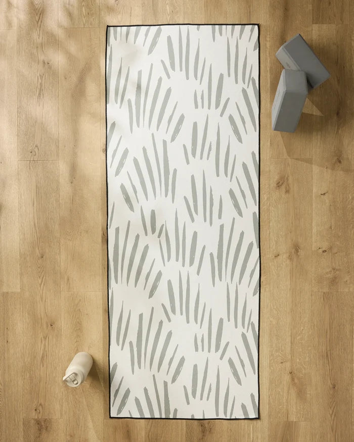 The Country Fields yoga mat by Hufton Studio, featuring gray abstract brushstrokes, rests on a light wood floor with a non-slip towel, water bottle, and two gray yoga blocks nearby for a serene workout space.