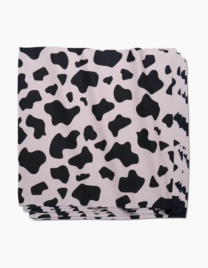 A stack of GEOMETRYs Cow Print Black Dinner Napkin Set, made from eco-friendly Geosuede fabric and featuring an irregular black and white cow print pattern.