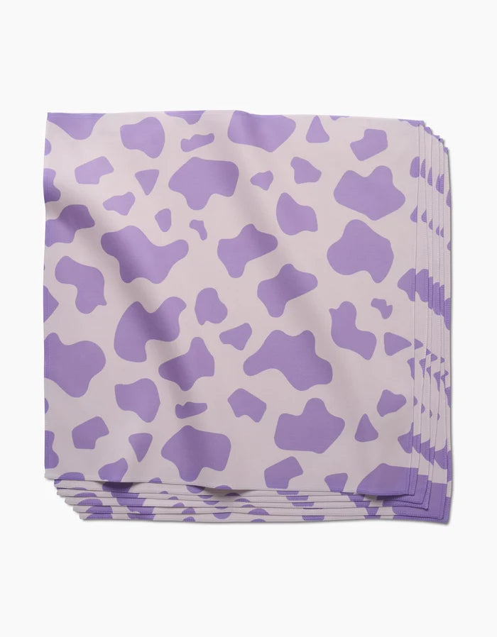 A neatly stacked set of GEOMETRY Cow Print Lilac absorbent cloth napkins featuring a light purple cow-print pattern on a pale background, displayed on a white surface.