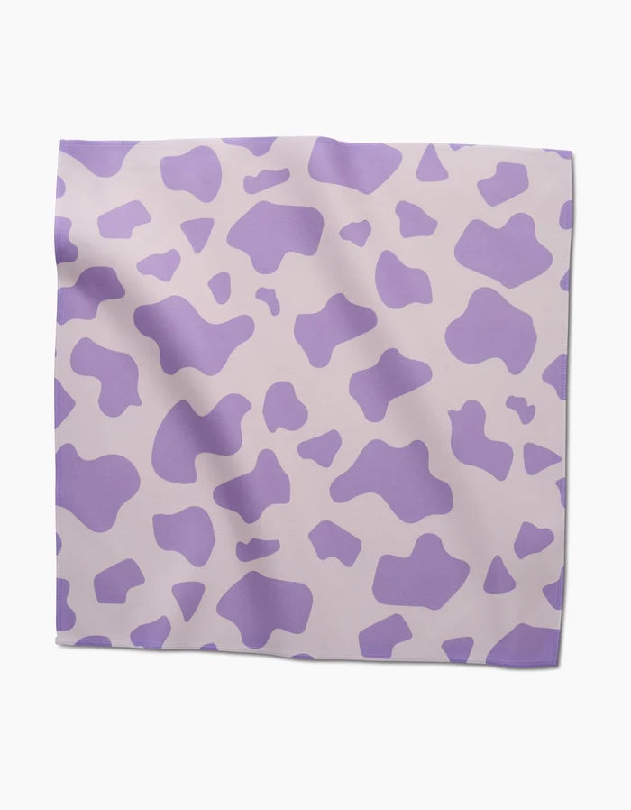 The GEOMETRY Cow Print Lilac is a square scarf with an abstract purple cow pattern on light beige, designed like chic, absorbent cloth napkins and shown flat on a white surface.