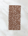 The Cowboy Horse Hide notebook by Hufton Studio, featuring a rectangular brown cover with a white speckled pattern, rests on a white marble surface next to an ultra-absorbent towel.