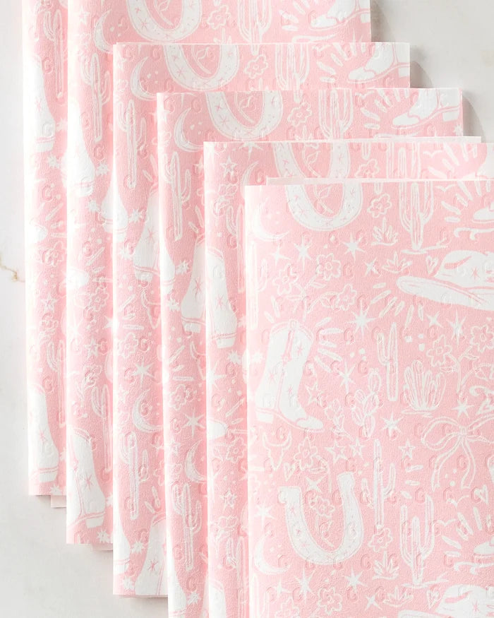 Five pink Cowgirl Chic napkins by Aubrey Fairchild, featuring white cowboy boots, cacti, horseshoes, and stars, are fanned out on a light surface—adding Western flair to your table as an eco-friendly option.