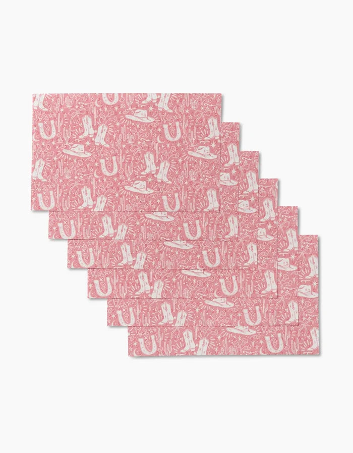 Six pink rectangular Cowgirl Chic placemats by Aubrey Fairchild, featuring white Western-themed patterns, are arranged in an overlapping formation on a white background. These reusable mats offer an eco-friendly alternative to Not Paper Towels.