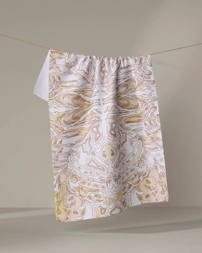 The Skye Walker "Crab" dish towel, featuring abstract symmetrical beige and white patterns, hangs on a clothesline against a neutral background.
