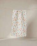 The GEOMETRY Crayon Floral ultra-absorbent white towel, featuring an orange and green floral design, hangs against a neutral beige background.