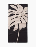 The Cream Monstera Bar Towel by PrintedPlant features a large beige monstera leaf on dark Geoweave fabric, offering superior absorbency and style.
