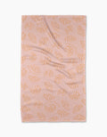 The Croissant Crush tea towel by Geometry, made from recycled materials, features orange croissants on pink and is shown laid flat against a white background.