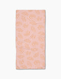 The Croissant Crush towel by Geometry is a pink rectangular bar towel with an all-over orange line-drawn croissant pattern, crafted from durable Geoweave fabric and displayed on a white background.