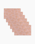 Six reusable Croissant Crush placemats by Geometry, featuring a pink background with orange croissants and polka dots, are stacked in a staggered overlap on a white surface.