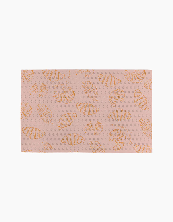 Introducing Croissant Crush by Geometry: a rectangular pink mat featuring orange croissants and repeating G letters on a light background, crafted from eco-friendly materials for a stylish, responsible update to your space.