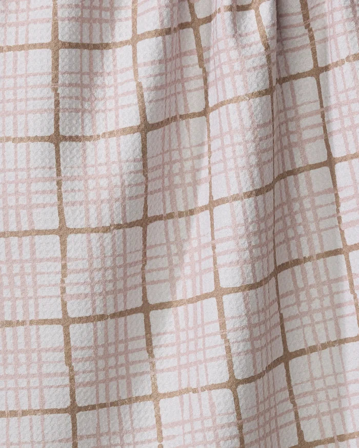 A close-up of the Studio Jeannot Crossover tea towel shows its ultra-absorbent, textured fabric with a grid of tan and light pink lines on white, slightly gathered at the top.