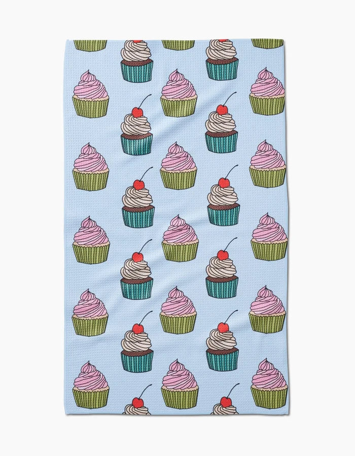 Cupcake Love by Amy Droubay is a light blue tea towel made from recycled materials, adorned with colorful cupcakes—featuring pink or white frosting, green or blue wrappers, red cherries on top, and a single cherry near the bottom edge.