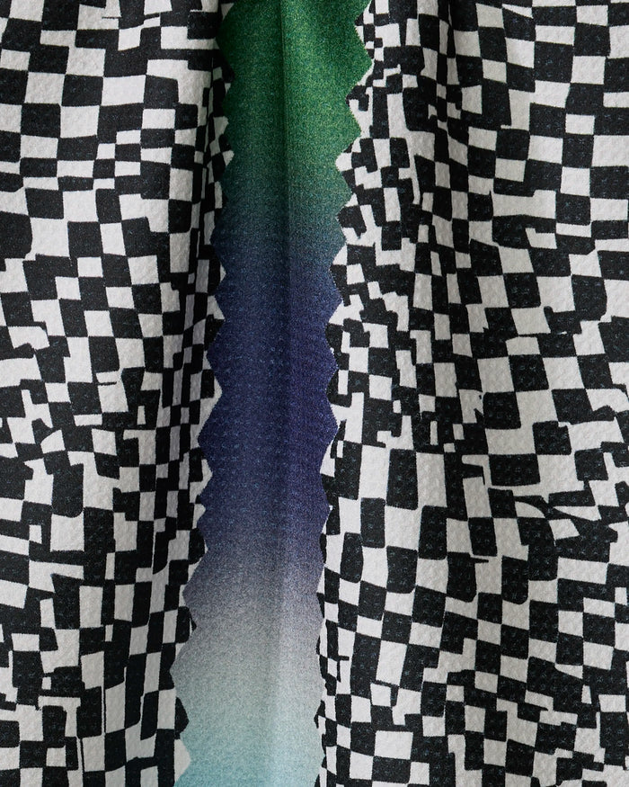 Close-up of Geometry’s “Current” tea towel with a black and white checkered pattern, jagged zigzag edge, and a green-to-blue-to-purple gradient. Made from quick-drying, recycled materials for eco-friendly use.