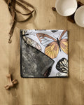 The Geometry Cute Butterflies dog towel lies folded on a wooden floor near two ceramic bowls, a brown leash, and a pair of dog bones.