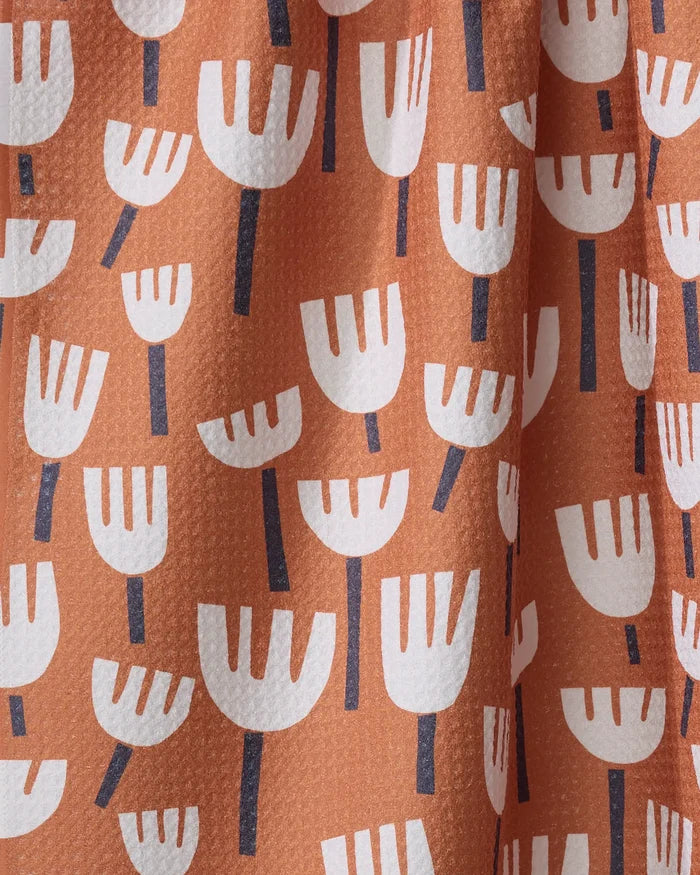 A close-up of the "Cutout Flowers" tea towel by Claire Iglesias in peach, with white abstract flower shapes and dark stems. Made from recycled materials, this ultra-absorbent kitchen towel has a slightly textured look.