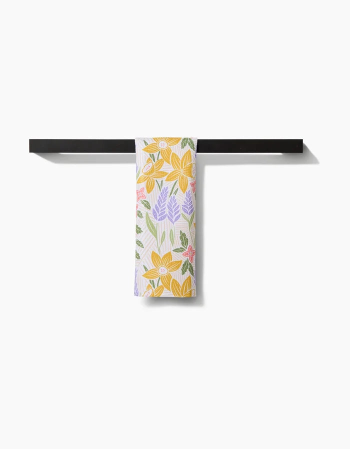 The Sarah Daugherty “Daffodil Dreams” Bar Towel, made from Geoweave fabric and featuring a floral design, is shown folded neatly over a black bar against a white background.