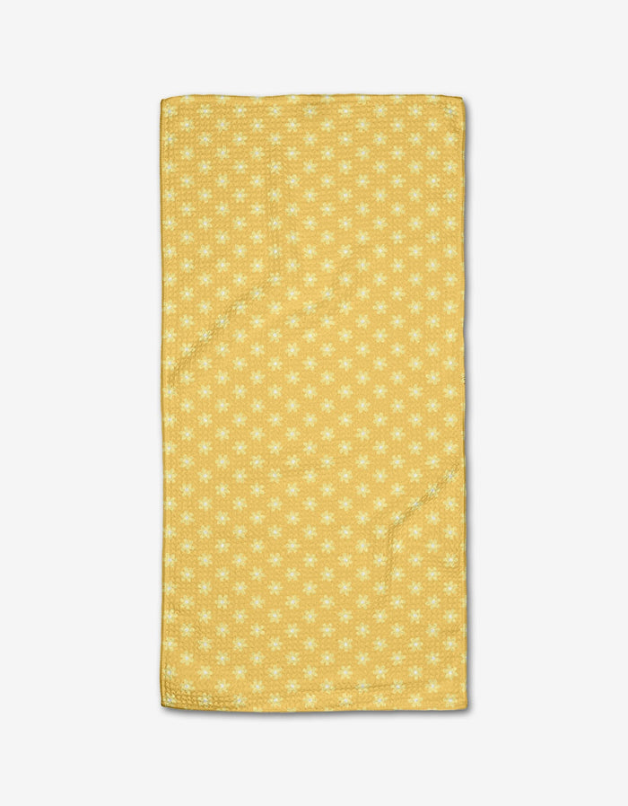The Rebecca Bobko Daisy Daze bar towel features a yellow background with small white flowers, crafted from ultra-absorbent Geoweave fabric and displayed on a white surface.